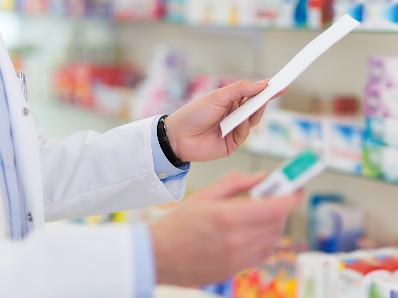 Pharmacien d'officine tenant une ordonnance et une boîte de médicaments